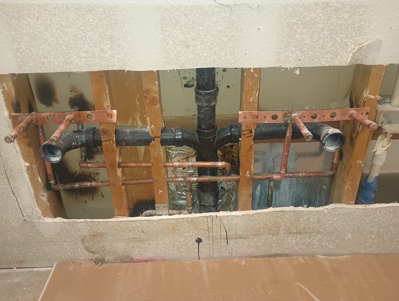 Copper and ABS rough-in plumbing laid out in a wall before drywall
