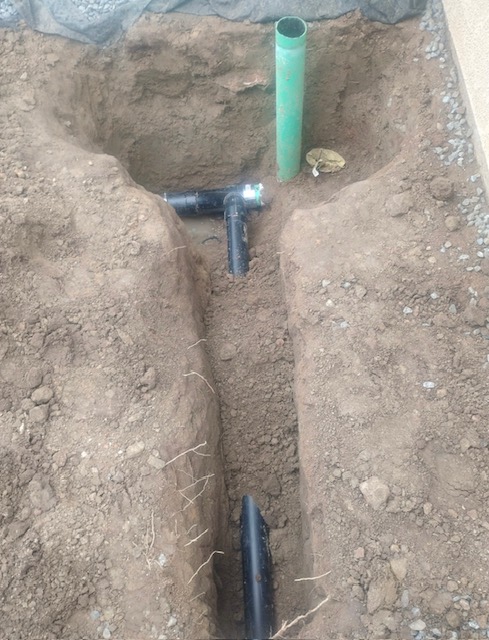 Black tee fitting and green pipe set in a trench